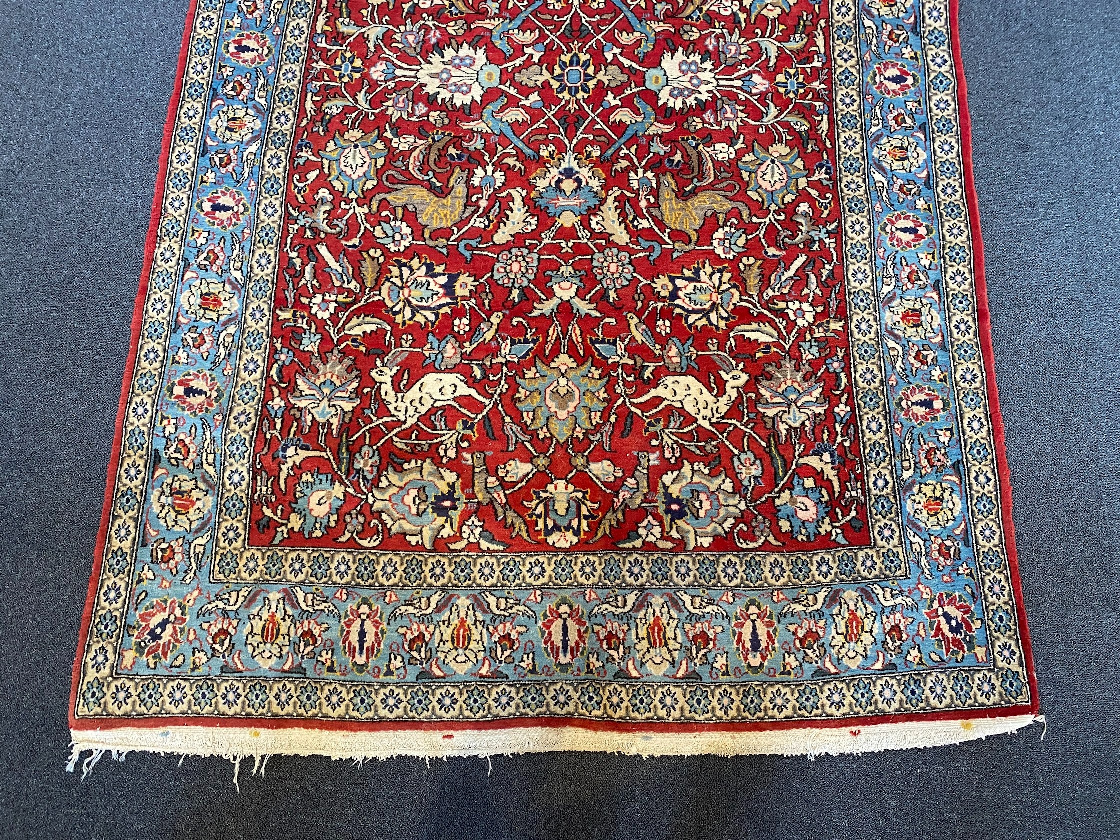 A Persian Qum red ground rug woven with animals and exotic birds among stylised flower heads 220 x 125 cms
